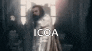 a man with a beard is standing in front of a window with the word icoa written on it .