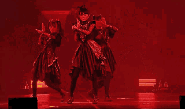 three girls in red dresses are dancing on a stage in front of a red background