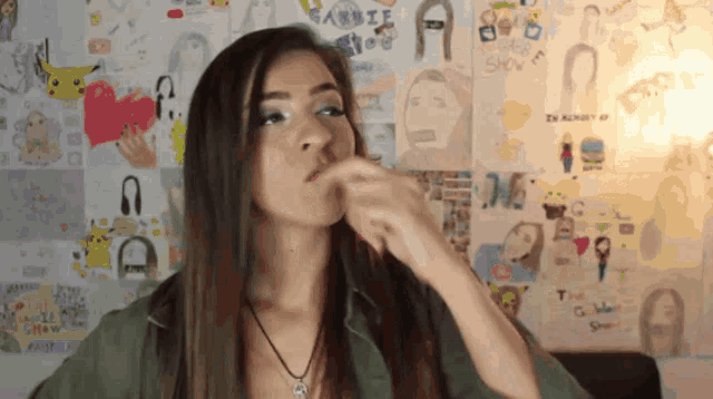 a woman covering her mouth with her hand in front of a wall with drawings of barbie