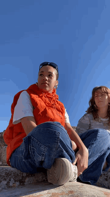 a woman in an orange vest sits next to another woman in jeans