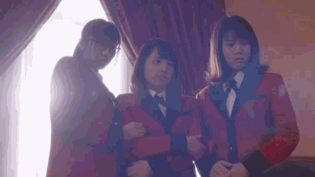 three women are standing next to each other in front of a window in a room .