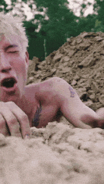 a shirtless man with a tattoo on his shoulder is laying in the dirt with his mouth open