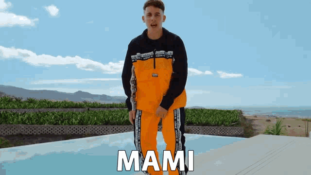 a man in a black and orange outfit is standing next to a pool and the word mami is on the bottom right