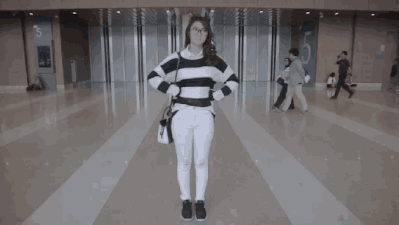 a woman in a black and white striped sweater stands in a hallway with people walking around