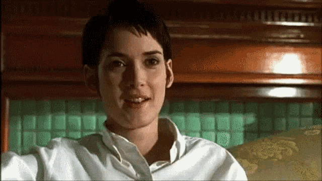 a woman in a white shirt is sitting on a couch and smiling .
