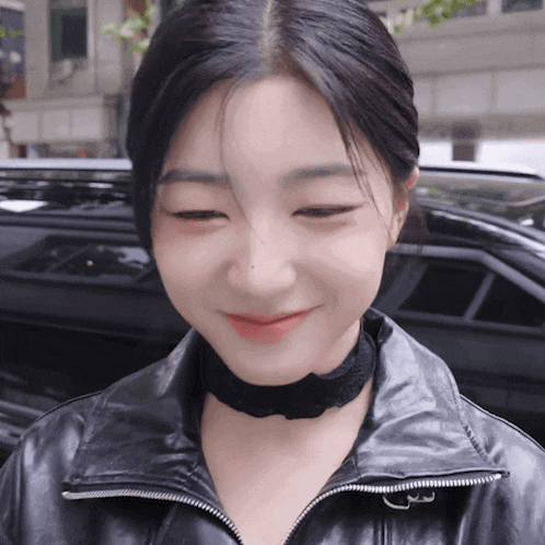 a woman wearing a black leather jacket and a black choker smiles for the camera