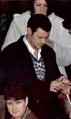 a man in a suit is sitting in a crowd of people and a woman is standing behind him .