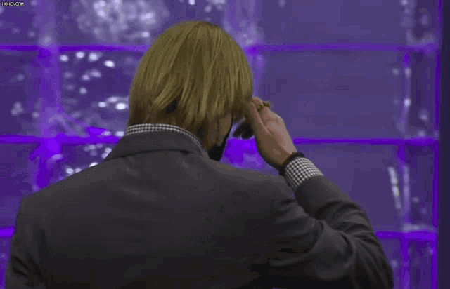 a man in a suit is standing in front of a purple wall and pointing