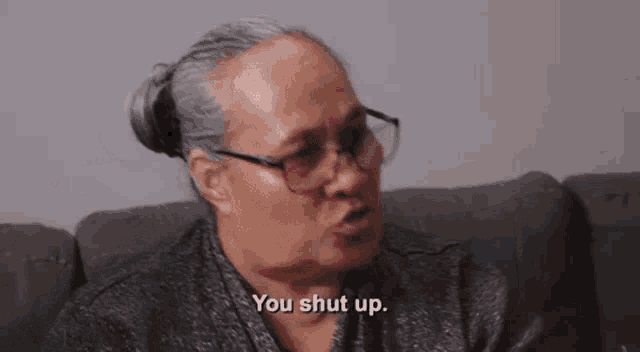 an elderly woman wearing glasses is sitting on a couch and talking .