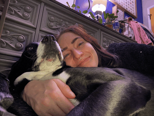 a woman is holding a black and white dog in her lap