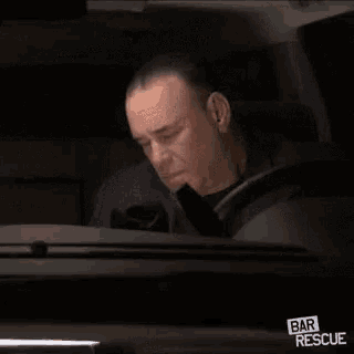 a man is sitting in the driver 's seat of a car and smoking a cigarette .