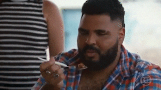 a man with a beard is eating food with a spoon while sitting at a table .