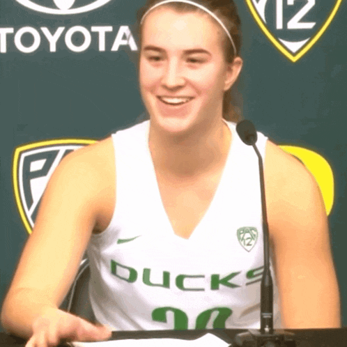 a woman wearing a ducks jersey sits in front of a toyota sign