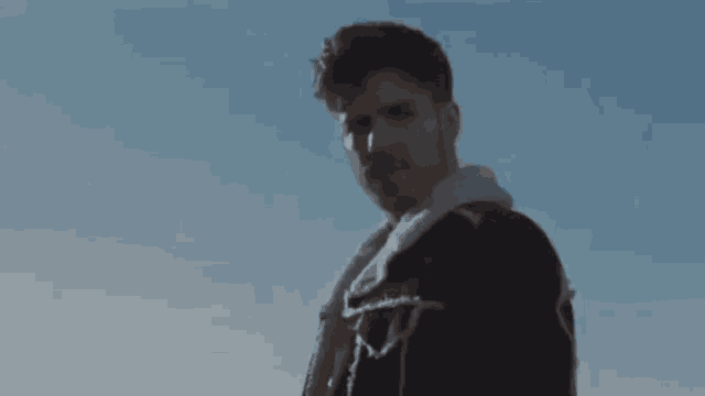 a man in a black jacket with a fur collar is standing in the desert .