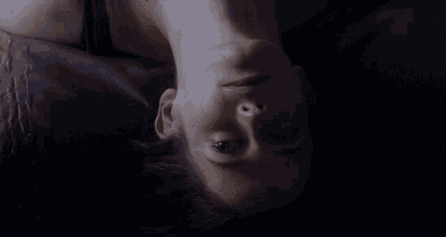 a woman is laying upside down on a bed with her eyes closed