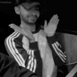 a man wearing a hat and a jacket is clapping his hands .