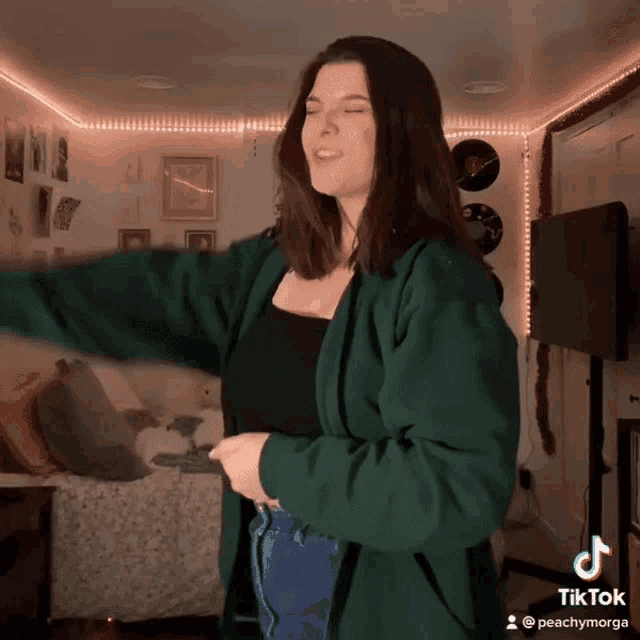 a woman in a green jacket is dancing in a room with tiktok written on the bottom right corner