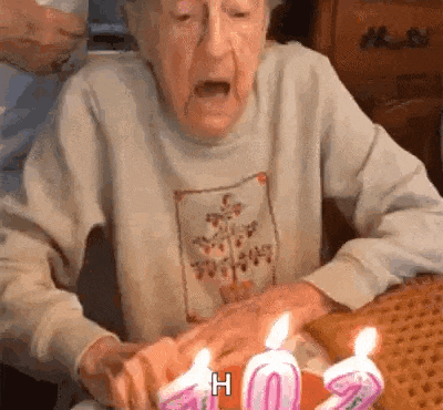 an elderly woman is blowing out her birthday candles on a cake .