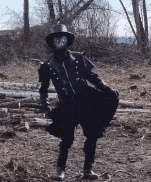 a person wearing a mask and a hat stands in a field of logs