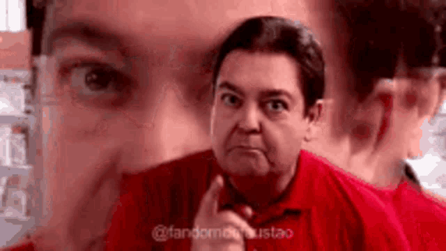 a man in a red shirt is making a funny face and looking at the camera .