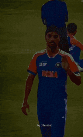 a man wearing a blue and orange india jersey stands on a field