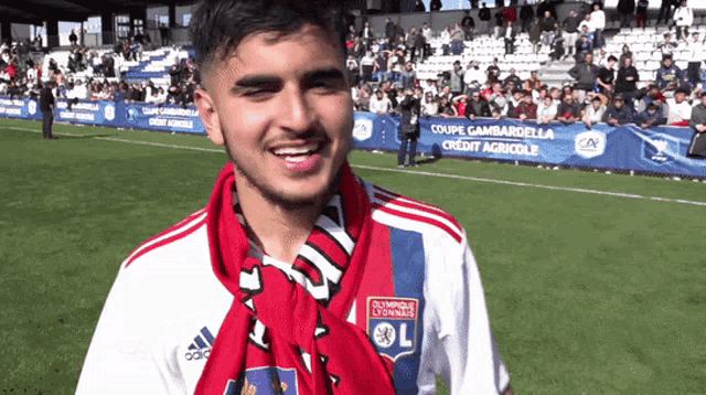 a young man wearing a olympique lyonnais jersey smiles on a soccer field