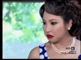 a woman wearing a polka dot dress and a pearl necklace is making a funny face .