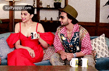 a man and a woman are sitting on a couch talking to each other and drinking coffee .