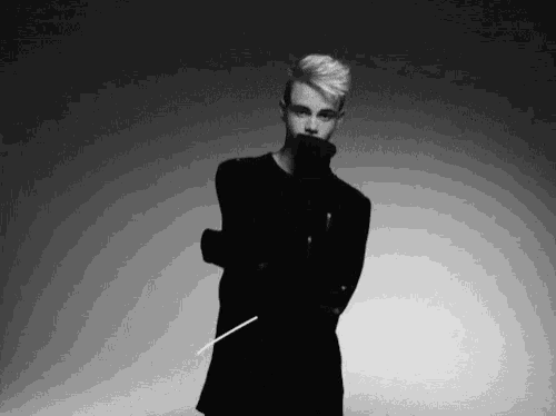 a black and white photo of a young man in a black coat holding a stick .