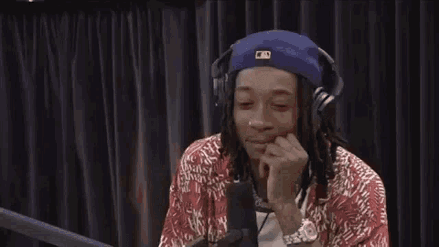 a man with dreadlocks is wearing headphones and a hat while sitting in front of a microphone .