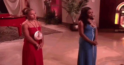 two women in dresses are standing next to each other in a living room .