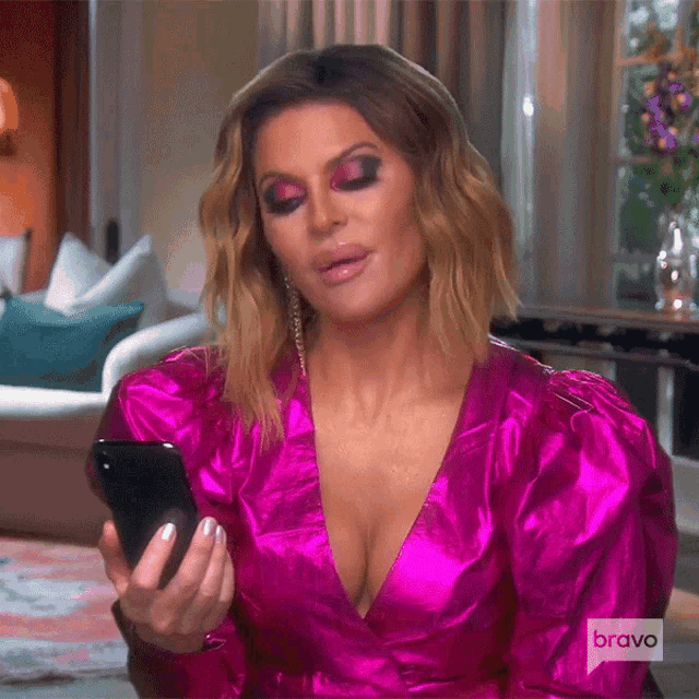 a woman in a pink dress is holding a cell phone in her hand .