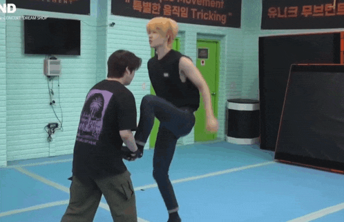 a man kicking another man in a gym with a sign above him that says tricking