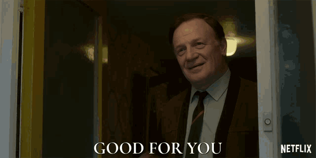 a man in a suit and tie is standing in front of a door that says good for you on it