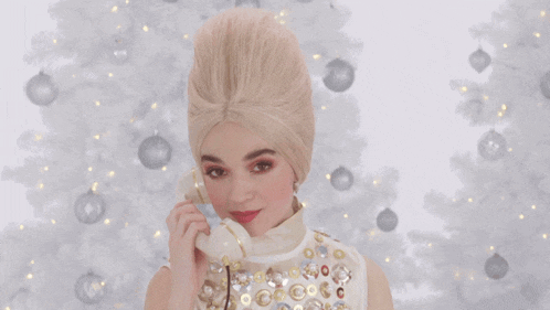 a woman in a wig is talking on a phone in front of a white christmas tree