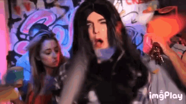 a man in a wig is dancing in front of two women in a room with graffiti on the wall .
