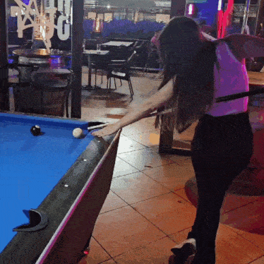 a woman is playing pool in front of a window that says tango