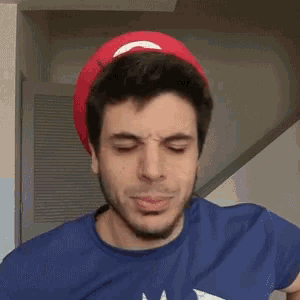 a man wearing a blue shirt and a red hat is making a face .