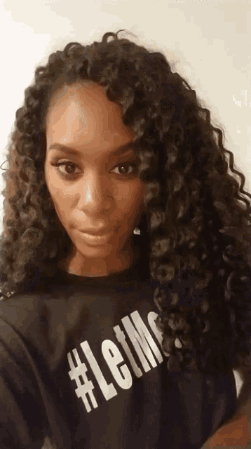 a woman with curly hair is wearing a black shirt that says #letm