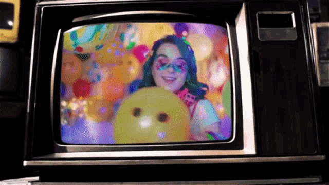 a tv screen shows a woman holding a yellow balloon with a smiley face on it