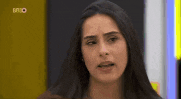 a woman with long dark hair is making a funny face while standing in front of a yellow wall .