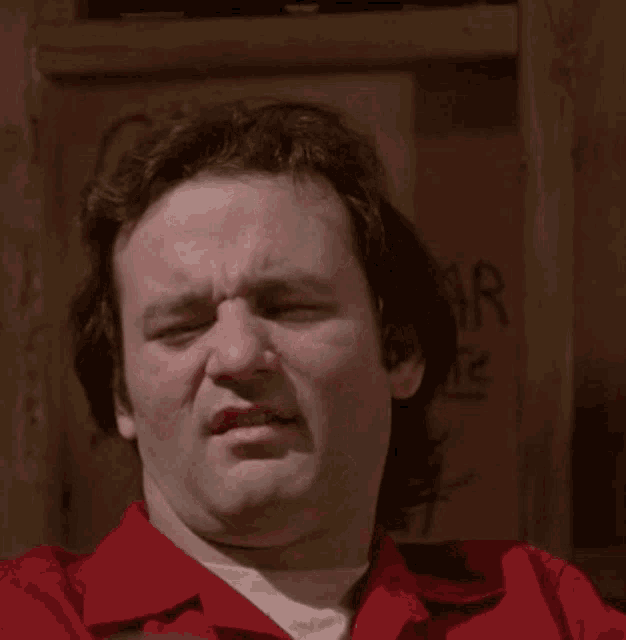 a man in a red shirt is making a funny face with his eyes closed and his mouth open .
