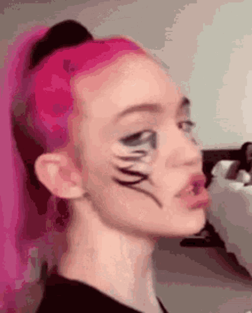 a woman with pink hair and makeup on her face is making a face .