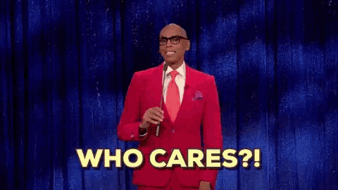 a man in a red suit and tie is standing on a stage holding a microphone and saying `` who cares '' .
