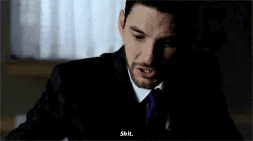 a man in a suit and tie is sitting in a dark room and talking on a cell phone .