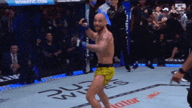 a man in yellow shorts is standing in a boxing ring with the word ufc on the floor