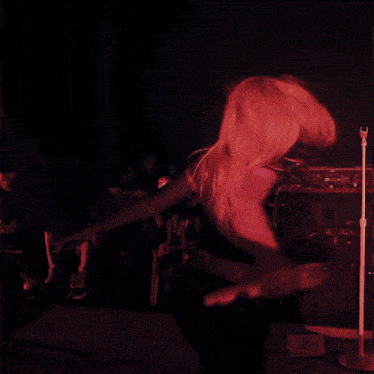 a woman is singing into a microphone while a man sits on a couch behind her