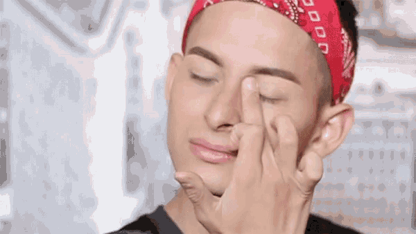 a man wearing a red bandana is touching his nose with his fingers .