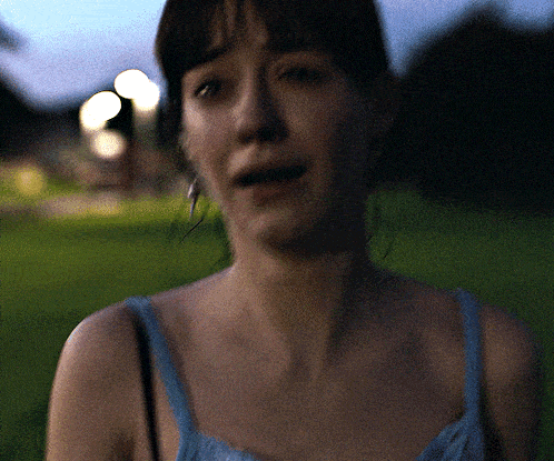a woman in a blue tank top is standing in the grass