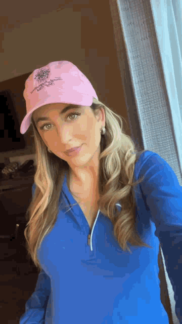 a woman wearing a blue shirt and a pink hat takes a selfie